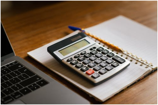 A calculator on a notepad with a pencil and a laptop