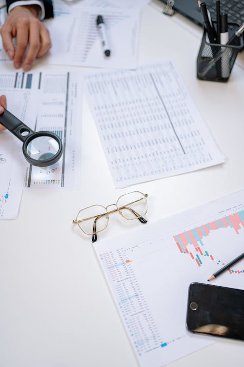 A person holding a magnifying glass over a document with other papers on the table