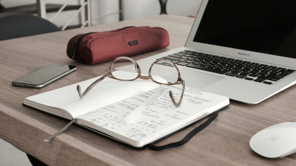 A notebook and pair of glasses in front of a laptop